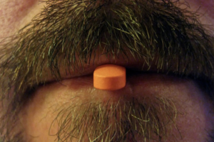 A man with facial hair's mouth appears with a single pill sticking out of it to compliment a letter written to Hypothyroidism and Synthroid for the Dear Diagnosis literary project.