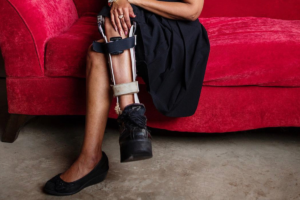A woman of color wears a leg brace as she sits regally upon a red couch. This image was submitted to accompany a letter written to Polio for Dear Diagnosis: a literary project in narrative medicine.