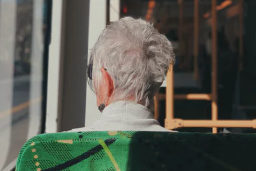 an older woman riding public transit, while looking out the window; which reflects the author's tone in her letter to CO-VID