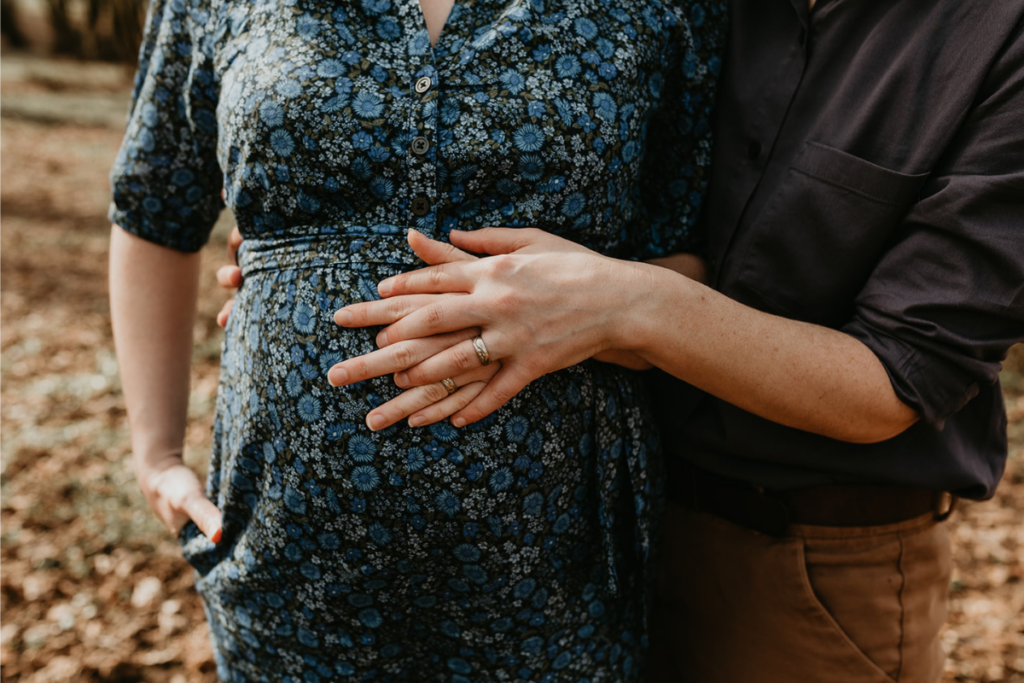 The ripe belly of a pregnant woman is presented with her wife's hands interlaced atop it, as selected by the courageous author whose letter to postpartum is featured at www.deardiagnosis.com.