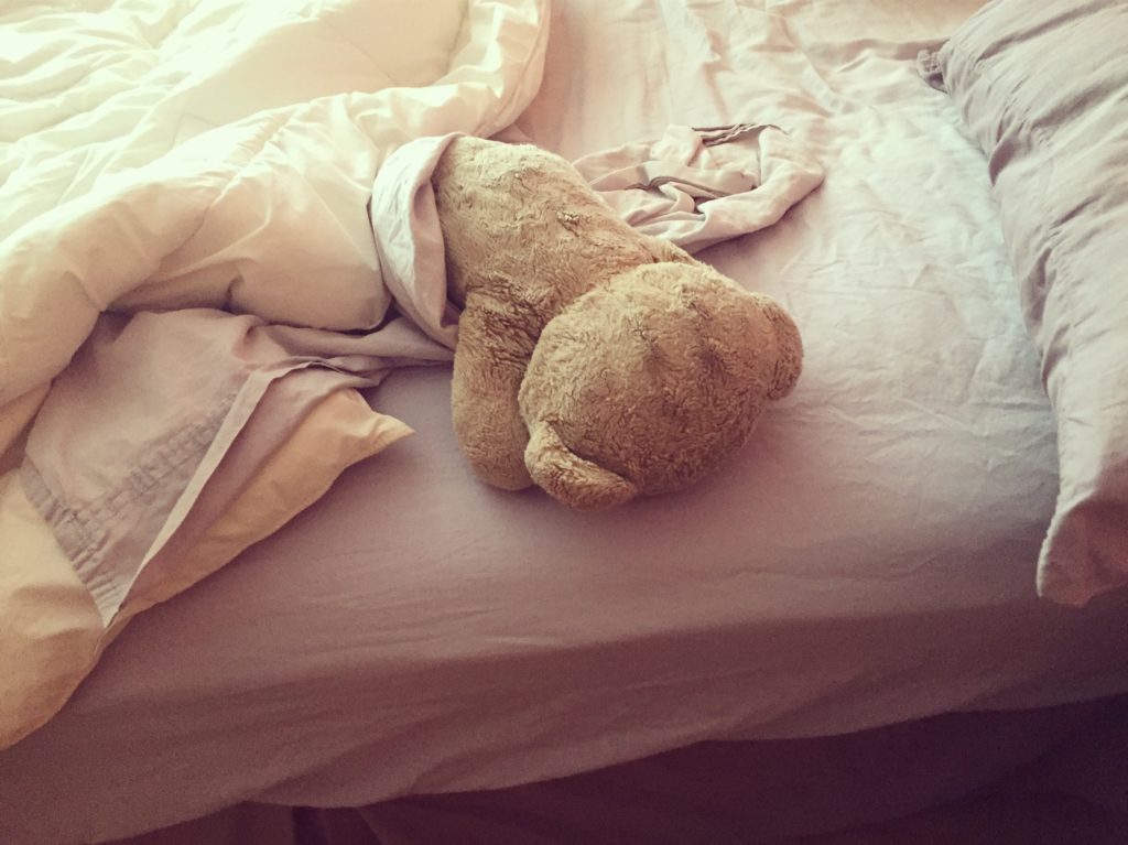 A teddybear lays face-down in a bed reflecting the tone of an author's letter written to idopathic hypersomnia